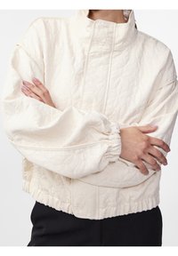 Pikowana kremowa kurtka z wysokim kołnierzem, oversize'owymi rękawami, elastycznymi mankietami i marszczonym dołem. Ozdobiona kwiatowym wzorem strukturalnym.