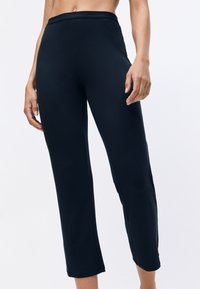 Leggings noirs stretch avec une taille haute, une texture lisse et un design fuselé, arborant un logo de marque subtil sur la ceinture.