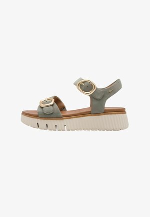 Zielona zamszowa sandał z dwoma złotymi okrągłymi klamrami, brązową wkładką oraz masywną białą podeszwą z rowkowaną fakturą.