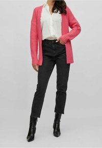 Růžový pletený svetr, bílá košile s knoflíky, černé džíny s vysokým pasem a černé kotníkové boty se zipem. Ležérní outfit s kombinací textur.