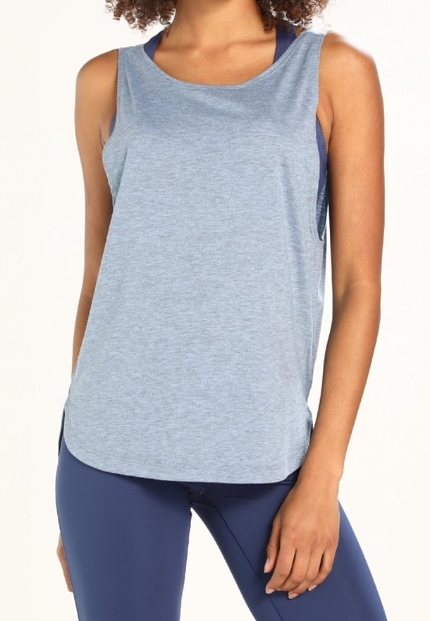 Femme portant un haut de sport sans manches bleu clair et des leggings bleu marine, debout avec une main reposant à côté de sa cuisse.