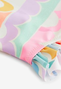 Färgg cloth med vågig design; innehåller pastelltoner av rosa, lavendel, grönt och orange. Inkluderar volangdetalj vid fållen.