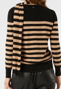 Černý a béžový pruhovaný svetr s dlouhými rukávy, kulatým výstřihem a detailem na zádech. Materiál působí měkce, s žebrovaným lemem a ladící šálou.