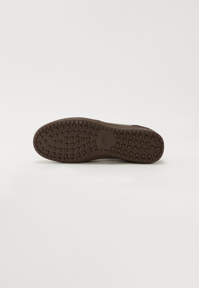 Semelle de chaussure en caoutchouc marron avec un motif de traction texturé, présentant des indentations carrées et un bord courbé lisse pour le confort et la stabilité.