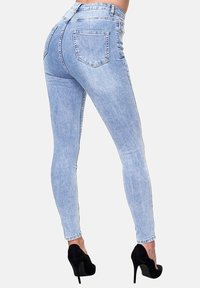 Jeans ajustados azul claro de mezclilla, con una cintura alta, dos bolsillos traseros y una textura suave. Combinados con tacones de aguja negros.