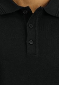 Schwarzes Polohemd aus Strickstoff, mit klassischem Kragen und drei schwarzen Knöpfen. Glatte Textur, schlichtes Design.