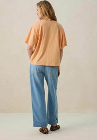 T-shirt en coton pêche avec un design ample, assortie à un jeans en denim bleu clair à jambes larges avec des ourlets retroussés et des chaussures slip-on à imprimé animal.