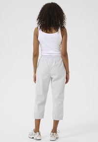 Vaaleansiniset raidalliset housut, joissa on joustovyötärö, lyhyt pituus ja pehmeä tekstuuri, yhdistettynä valkoiseen toppiin ja lenkkareihin.