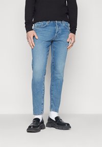 Világoskék, slim fit farmernadrág, öt zsebes kialakítással és enyhe elhalványulással, fekete lófarokkal és fehér zoknival párosítva.