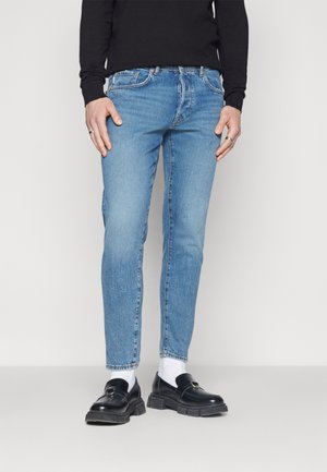 Light blue denim jeans with a slim fit, featuring a five-pocket design and subtle fading, paired with black loafers and white socks.