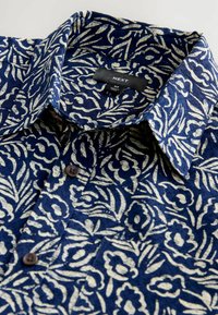 Kurzarmhemd aus navyblauem Stoff mit weißen Blumenmustern, Knopfschluss und spitzem Kragen. Markenlabel innen sichtbar.