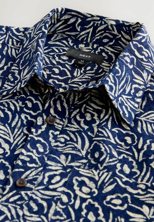 Short-sleeve shirt featuring a navy blue fabric with a white floral pattern, button closure, and a pointed collar. Brand label visible inside.