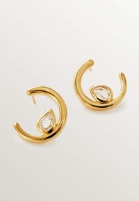 Pendientes en tono dorado con un diseño curvado, que presentan una piedra clara en forma de pera acentuada dentro de la curva. Acabado suave, forma moderna.