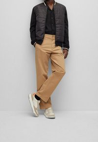 Svart puffig bomberjacka med vit och orange randig krage, i kombination med tan chinos och beige sneakers med orange accenter.