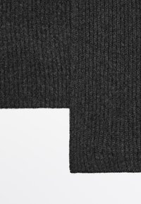 Tissu tricoté gris foncé avec une texture côtelée, montrant un bord marqué où le tissu rencontre un fond blanc, soulignant son épaisseur.