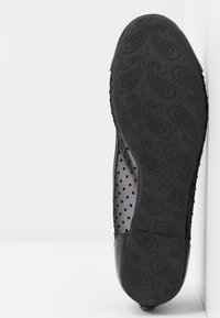 Semelle de chaussure noire avec motif cachemire sur la bande de roulement, indiquant la taille 37, sur un fond blanc incliné verticalement.