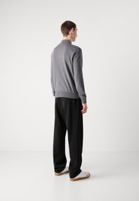 Cardigan grigio a maglia con colletto, polsini e orlo a coste, abbinato a pantaloni neri e sneakers bianche. Modello mostrato di spalle.