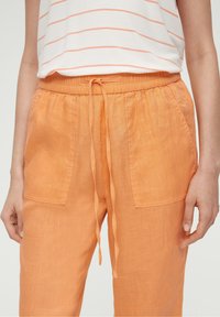 Oranje linnen broek met een elastische tailleband en een trekkoord, twee zijzakken en een lichte, gestructureerde stof.