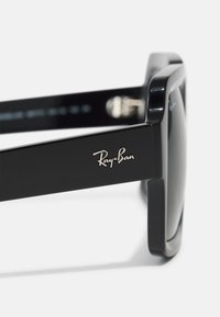 Ochelari de soare Ray-Ban negri, cu ramă dreptunghiulară, având lentile întunecate și un logo argintiu pe lateral. Textură netedă din plastic.