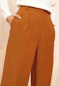 Rood-oranje broek van een zachte stof, met plooien, zijzakken en een getailleerde pasvorm. Inclusief een gestructureerde tailleband voor vorm.