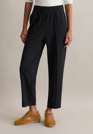 Zwarte, elastische tapered broeken met voorplooien, gecombineerd met bruine sneakers met roze accenten en gestructureerde veters.