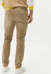 Vaqueros ajustados de color marrón claro con cinco bolsillos, costura sutil y etiqueta de parche en la cintura trasera. Combinados con zapatillas blancas.