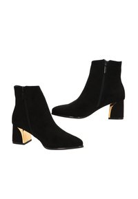 Botas de tobillo de ante negro con punta afilada, cremallera lateral y un tacón cuadrado con detalles en dorado. Textura suave y diseño elegante.