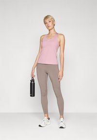 Rosa treningssinglet med rund hals, kombinert med lyse brune leggings. Personen holder en svart vannflaske. Hvite treningssko.
