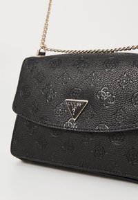 Sort textured læderhandtaske med klaplukning, der har et præget logo-mønster og et trekantet metalmærke på forsiden.