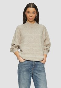 Licht beige gebreide trui met een hoge ronde halslijn, een relaxte pasvorm en opgerolde mouwen, gecombineerd met blauwe denim jeans.