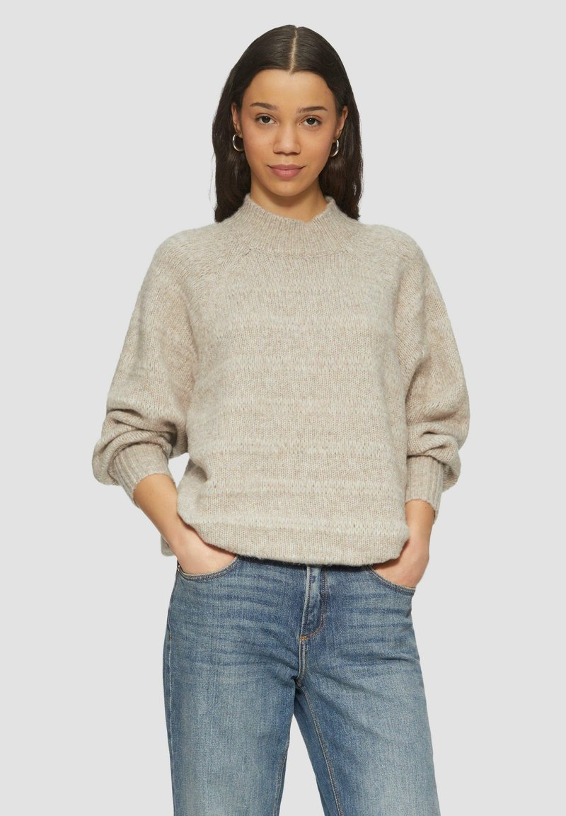 Licht beige gebreide trui met een hoge ronde halslijn, een relaxte pasvorm en opgerolde mouwen, gecombineerd met blauwe denim jeans.