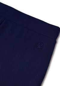 Tmavě modrá žebrovaná látka, kalhoty s rovnou pasovkou a jemně vyšívaným logem. Hladká textura s přiléhavým střihem.