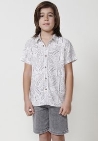 Trumpas rankovėmis balta marškiniai su pilkais lapų raštais, užsegami sagomis; derinami su pilkais džinsiniais šortais. Lygus paviršius, laisvas kirpimas.