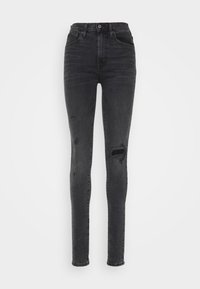 Jeans negros ajustados de cintura alta con detalles desgastados y lavado descolorido en los muslos y las rodillas, diseño de cinco bolsillos y cierre de botón.