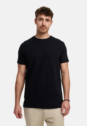 Camiseta de algodón negra de manga corta, cuello redondo y corte recto, combinada con pantalones beige. Textura suave sin patrones visibles.