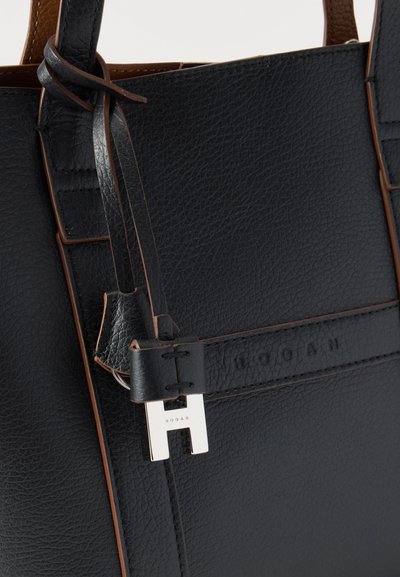 Μαύρη δερμάτινη τσάντα με υφή και καφέ άκρες, με ασημένιο διακοσμητικό "H" και ανάγλυφη σήμανση "HOGAN" στο μπροστινό λουράκι.