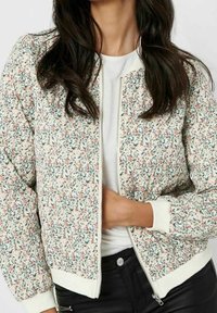 Veste bomber fleurie avec un fond clair, présentant de petits motifs rose et vert, des poignets côtelés et une fermeture éclair frontale.