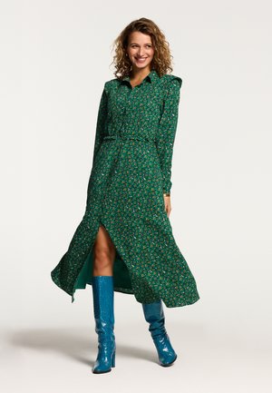 Abito lungo a maniche lunghe floreale verde con colletto abbottonato, vita arricciata e spacco laterale, abbinato a stivali blu lucidi al ginocchio.