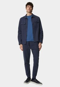 Navy blauw sweatsjack met twee voorzakken, gedragen over een bijpassend crewneck shirt en tapered sweatpants, gecombineerd met zwarte sneakers.