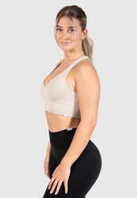 Beige geribbelde sportbeha met een V-hals en brede banden, gecombineerd met hoge zwarte legging die een brede tailleband heeft.