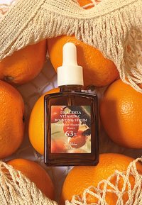 Botella de vidrio marrón con una tapa gotero blanca, con una etiqueta colorida. Rodeada de naranjas brillantes y una bolsa de malla crema.