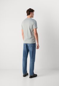 Camiseta de manga corta gris claro con cuello redondo, combinada con jeans de mezclilla azul. Los jeans presentan un corte recto y un leve desgaste.