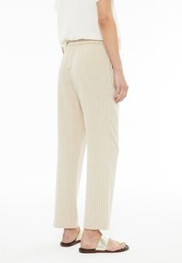 Pantalones de pierna ancha de canalé en color beige con cintura elástica, que cuentan con una textura suave y un corte recto, combinados con sandalias planas minimalistas.