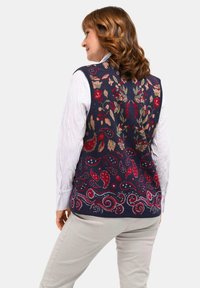 Gebreide vest in marineblauw met rode, groene en crème bloem- en paisleypatronen. Heeft een hoge halslijn en is mouwloos.