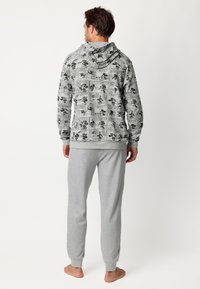Sudadera con capucha en gris con patrones de cómic, acompañada de pantalones de chándal gris claro. El material parece suave, con puños y dobladillo acanalados.