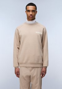 Sudadera beige con cuello alto, puños acanalados y detalle de logo en el pecho. Textura suave y corte relajado, combinada con pantalones a juego.