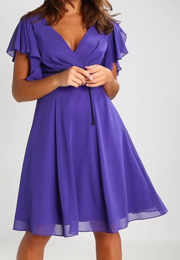 Robe violette avec un décolleté en V et des manches volantées. Fabriquée dans un tissu léger avec une jupe fluide et un lien à la taille. Texture douce.