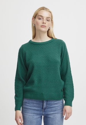 Pulover verde tricotat cu un model texturat, guler rotund și manșete cu nervuri. Asortat cu blugi albaștri pentru un look casual.