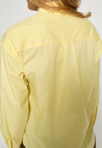 Gul skjorte med knapper, der har et bagstykke med bærestykke og læg, lavet af blødt bomuldsstof med lange ærmer og manchetter.