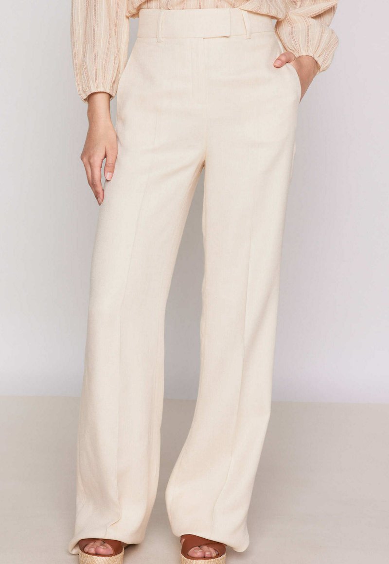 Pantaloni a gamba larga in tessuto beige chiaro. Presentano una texture liscia, vita alta con passanti per cintura e pieghe ben stirate su ciascuna gamba.